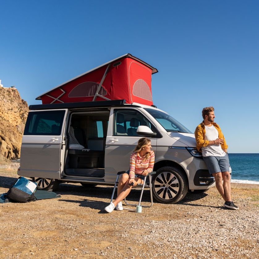 Ein Volkswagen California an einem Strand mit ausgefahrenem Aufstelldach