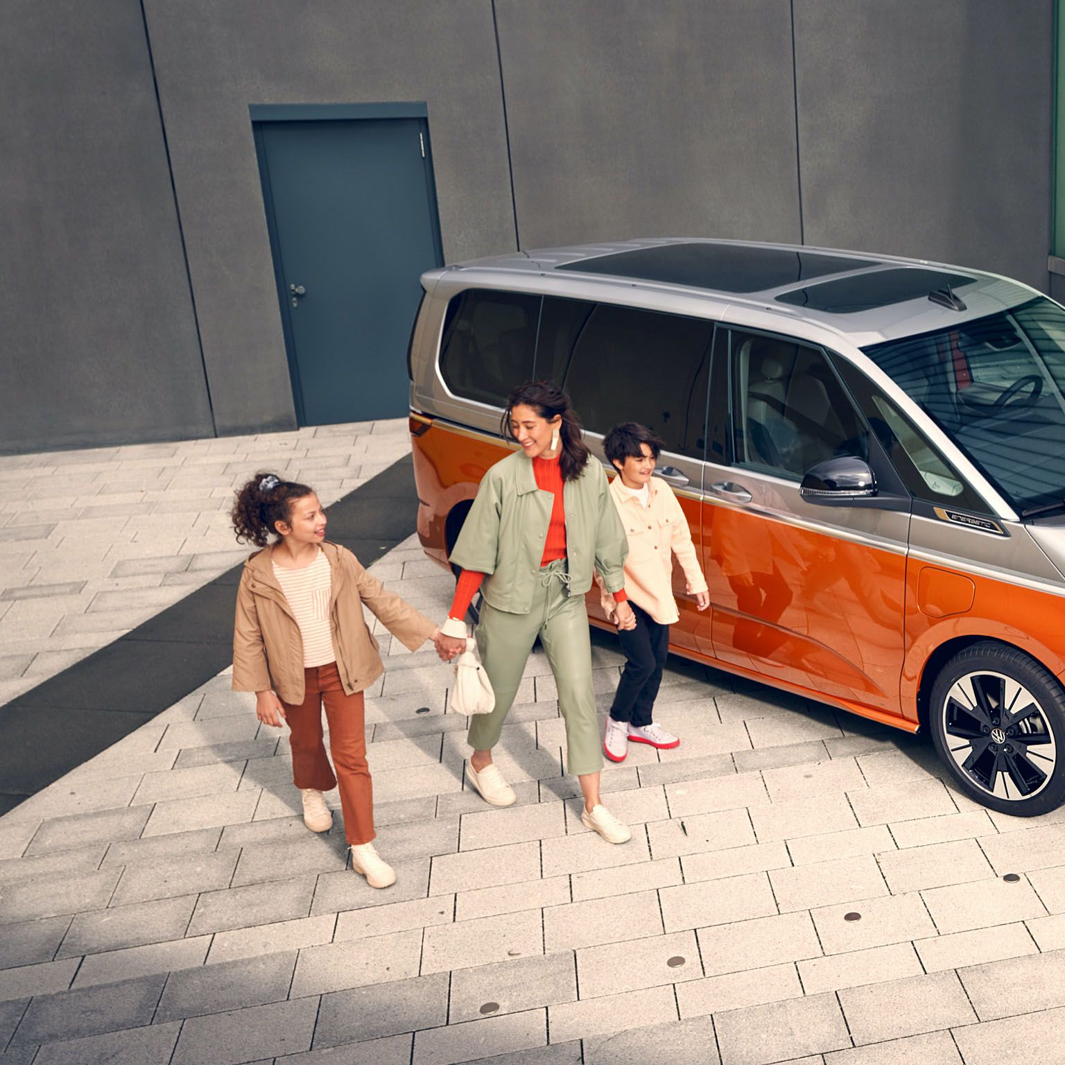 Eine Familie läuft vergnügt neben dem stehenden VW Multivan Energetic T7 2021 her