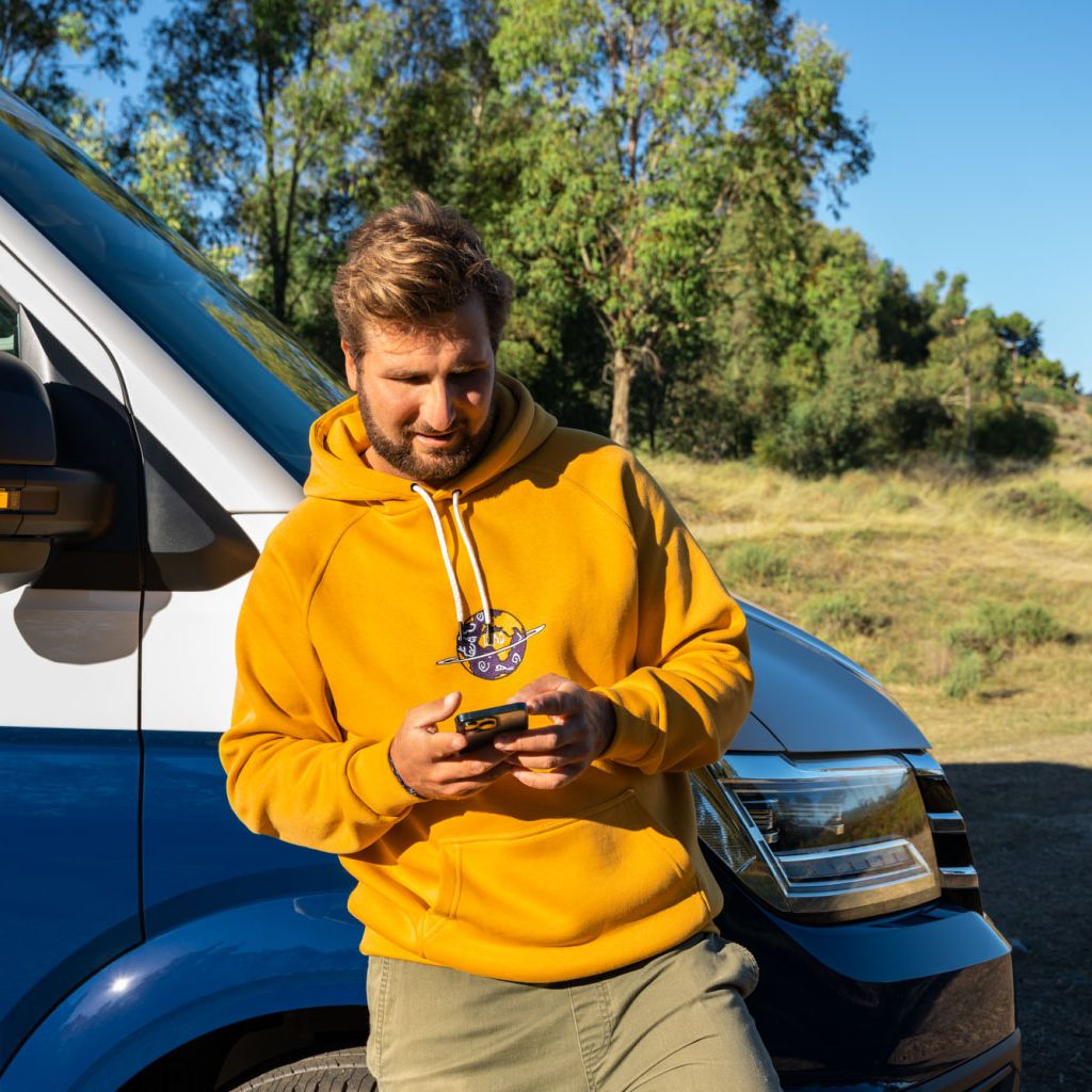 Ein Mann lehnt an seinem VW Nutzfahrzeug und blickt auf sein Smartphone