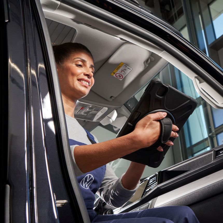 Eine Volkswagen Service Technikerin sitzt in einem Volkswagen Nutzfahrzeug und blickt auf ein Tablet.