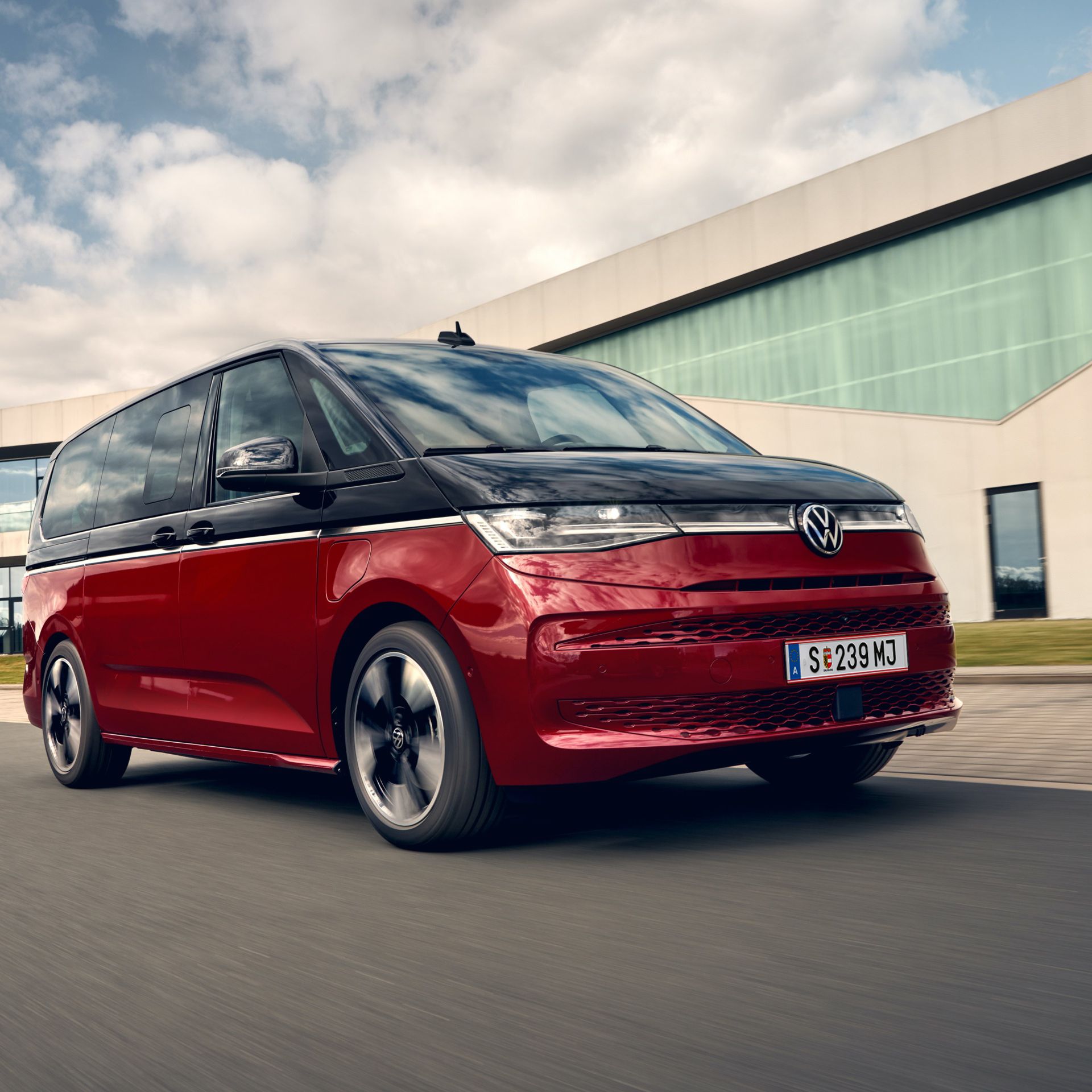 Der VW Multivan Style T7 2021 vor einem Gebäude aus Glas. 