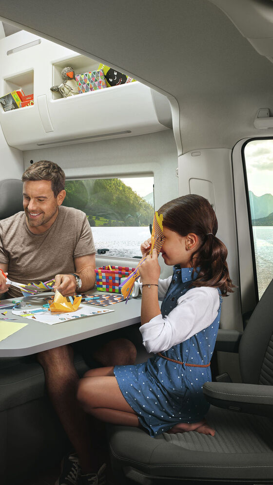 VW Grand California mund të shihet nga brenda. Një familje është e ulur së bashku në tavolinë. 